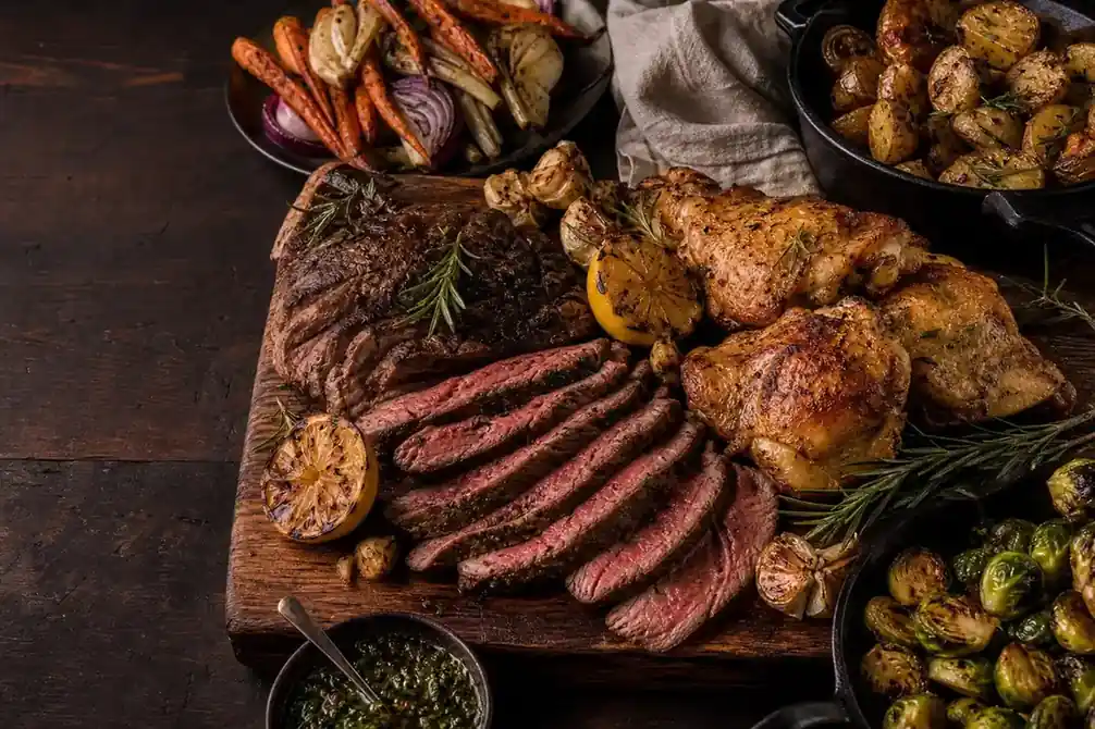 A generous table of grilled steak, chicken, vegetables, and herbs